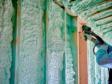 Photo for Builder insulating wooden frame house. Close up view of man worker spraying polyurethane foam inside of future cottage, using plural component gun. Construction and insulation concept. - Royalty Free Image