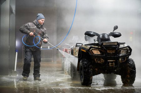 Volle Länge des Mannes Reinigung Quad-Fahrrad mit Hochdruck-Wassersprüher an SB-Waschanlage