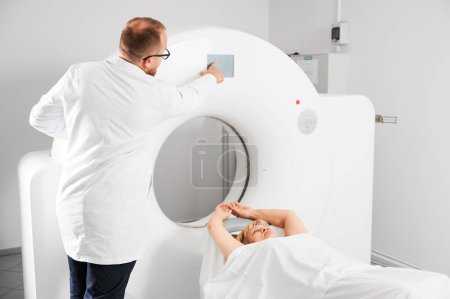 Téléchargez les photos : Tomodensitométrie médicale ou scanner IRM. Vue arrière du radiologue masculin appuie sur le bouton IRM pour examiner le patient féminin. - en image libre de droit