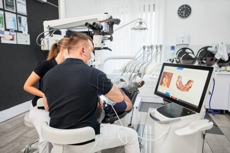 Dentist scanning patients teeth with modern machine for intraoral scanning. Digital print of patients teeth is on big screen. Modern high precision technologies. Concept of modern dentistry