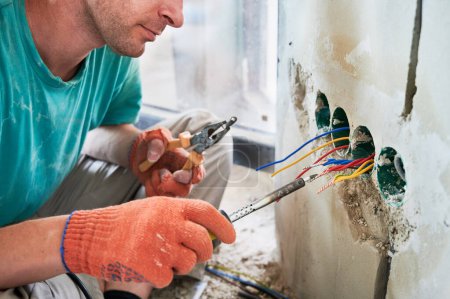 Photo for Close up of man in work gloves using welding repair tool while installing electric cables in apartment under renovation. Man holding pliers tool and melting tip of electrical wire with soldering iron. - Royalty Free Image
