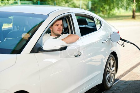 Téléchargez les photos : L'homme qui attend sa voiture sera ravitaillé. Homme confiant regardant par la fenêtre de l'auto si réservoir est rempli. - en image libre de droit