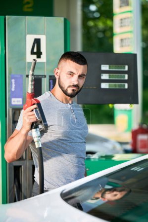 Geschickter Fahrer betankt sein Auto für lange Strecken. Porträt eines erwachsenen Mannes mit Pumpendüse, die Autotank betankt. Mann hält Benzinpumpe neben Auto an Gassäule.