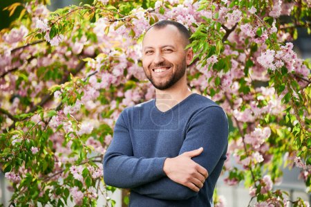 Man allergic enjoying after treatment from seasonal allergy at spring. Portrait of happy bearded man smiling in front of blossom tree at springtime. Spring allergy concept.