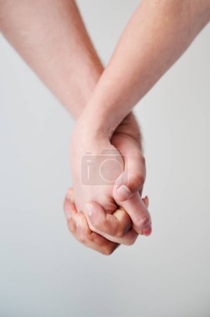 Two hands held together in grasp against neutral background. Close up of mans and womans hand. Concept of intimacy, support, and trust.