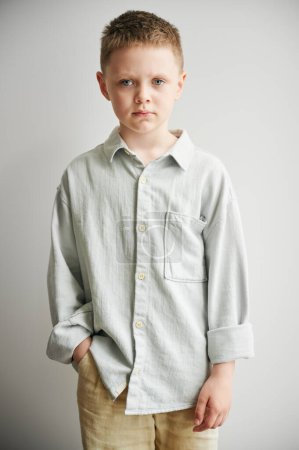 Porträt eines traurigen Jungen, der die Hand in der Tasche hält und in die Kamera blickt. Ernstes Kind in lässiger Kleidung posiert auf weißem Hintergrund.