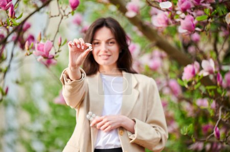 Eine Frau, die an einer saisonalen Allergie im Frühling leidet, posiert im blühenden Garten. Konzentrieren Sie sich auf die Hand einer Frau, die Allergien zeigt und eine Packung Tabletten in der Hand hält. Antihistaminisches Medikamentenkonzept