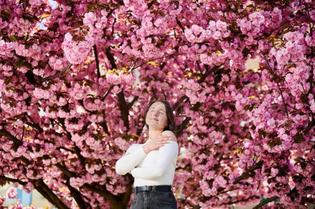 Woman allergic enjoying after treatment from seasonal allergy at spring. Portrait of happy beautiful woman with eyes closed in front of blooming sakura tree at springtime. Spring allergy concept.
