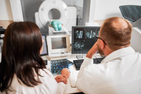 Tomodensitométrie médicale ou scanner IRM. Vue arrière de deux médecins assis, travaillant à l'ordinateur, faisant IRM. Deux spécialistes qui consultent, parlent, pensent, regardent. Concept de diagnostics modernes.