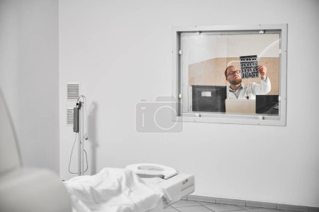 Tomodensitométrie médicale ou scanner IRM. Docteur assis à l'ordinateur, examinant les résultats de l'IRM. Spécialiste masculin portant des lunettes et uniforme, tenant le balayage, étudiant. Concept de médecine et d'hôpital.