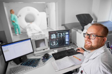 Medical computed tomography or MRI scanner. Doctor smiling to camera, nurse making MRI. Specialists working in hospital, doctor examiing, studying results on computer. Concept of modern diagnostics.