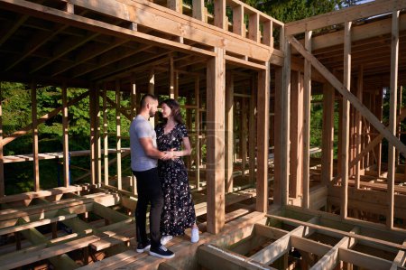 Photo for Man and woman appraising their future wooden frame dwelling nestled near the forest. Youthful couple at construction site in early morning. Concept of contemporary ecological construction. - Royalty Free Image