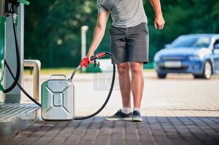 Handlicher Fahrer tankt Kanister mit Benzin an moderner Tankstelle. Mann füllt Zisterne mit Kraftstoff im Falle unvorhergesehener Umstände. Ausgeschnittene Ansicht eines Mannes mit Pumpendüse im Hintergrund seines Autos