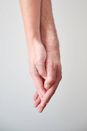 Close up view of hands of sweet couple. Young man and woman holding hands on light neutral background. Concept of love, intimacy, support, and trust.