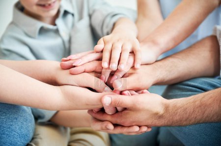 Photo for Close-up of several hands placed on top of one another in stack. Big family putting stacked hands together promising work in team. All family members showing their support to each other. - Royalty Free Image