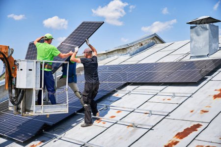 Trabajadores que levantan el panel solar fotovoltaico en la azotea de metal de la casa con la ayuda de grúa elevadora. Los hombres instaladores instalan módulos solares fotovoltaicos al aire libre. Concepto de generación de energía renovable.