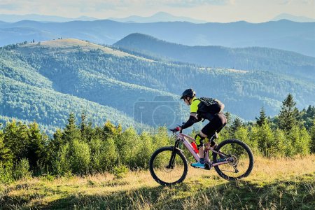 Radler Mann fährt Elektro-Mountainbike im Freien. Männliche Touristen radeln auf grasbewachsenen Wegen in den Bergen, tragen Helm und Rucksack. Konzept aus Sport, aktiver Freizeit und Natur.