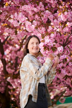 Photo for Woman allergic enjoying after treatment from seasonal allergy at spring. Portrait of happy beautiful woman smiling in front of blooming sakura tree at springtime. Spring allergy concept. - Royalty Free Image