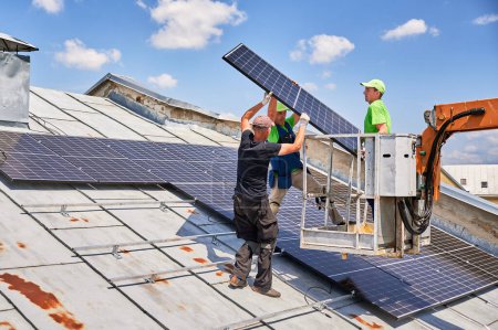Trabajadores que levantan el panel solar fotovoltaico en la azotea de metal de la casa con la ayuda de grúa elevadora. Los hombres instaladores instalan módulos solares fotovoltaicos al aire libre. Concepto de generación de energía renovable.