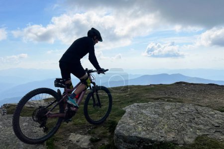 Cyclist man riding electric mountain bike outdoors. Silhouette male tourist biking along grassy trail in the mountains, wearing helmet. Concept of sport, active leisure and nature.
