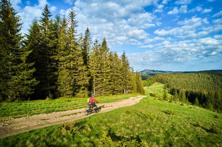 Cyclist man riding electric mountain bike outdoors on sunny day. Male tourist biking along grassy trail in the mountains, wearing helmet and backpack. Concept of sport, active leisure and nature.