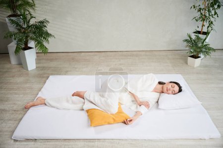 Schöne Frau entspannt sich nach Thai-Massage mit geschlossenen Augen auf Matte liegend.