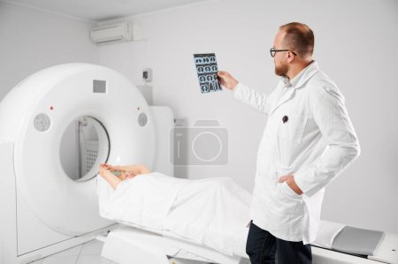 Medical computed tomography or MRI scanner. Doctor holding and examining results of MRI. Woman patient lying on couchette. Concept of medicine, healthcare and modern diagnostics.
