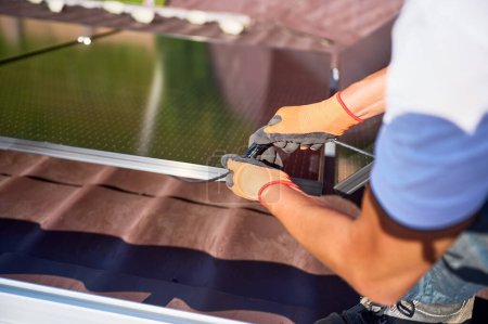 Téléchargez les photos : Travailleur installant le système de panneau solaire sur le toit de la maison. Fermer les modules de connexion électricien ensemble pour produire de l'électricité par effet photovoltaïque. Concept d'énergies alternatives et renouvelables - en image libre de droit