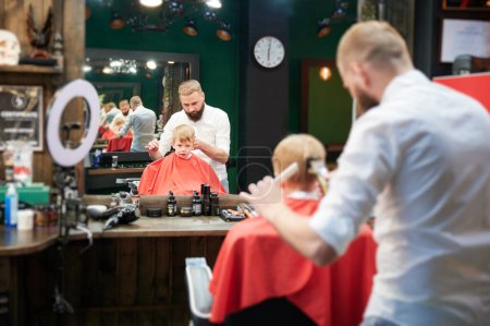 Téléchargez les photos : Barber en utilisant peigne et rasoir pour couper les cheveux. Coiffeur professionnel rasage petite nuque enfants. - en image libre de droit