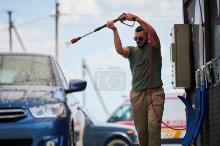Téléchargez les photos : Confident man washing his car on self car-washing station. Cleaning car using active foam. Young man cleaning his auto by water gun. - en image libre de droit