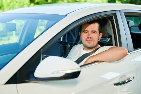 Téléchargez les photos : Adult man looking through window of his car. Confident man looking straight into the camera while sitting in white car. - en image libre de droit