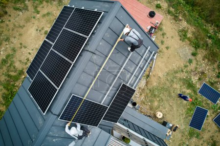 Téléchargez les photos : Builders measuring solar panels with tape measure. Aerial view of workers taking measurements before mounting solar modules on roof of house for generating electricity through photovoltaic effect. - en image libre de droit