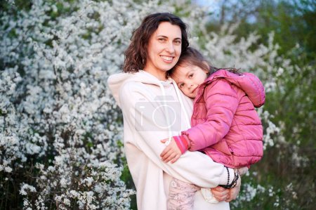 Téléchargez les photos : Woman and child allergic enjoying after treatment from seasonal allergy at spring. Happy mother holding young daughter smiling in front of blossom tree at springtime. Spring allergy concept. - en image libre de droit