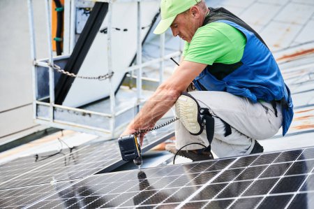 Arbeiter beim Bau einer Photovoltaik-Solaranlage auf dem Metalldach des Hauses. Techniker installieren Solarmodul mit Hilfe von elektrischen Bohrmaschine im Freien. Alternatives Energieerzeugungskonzept.