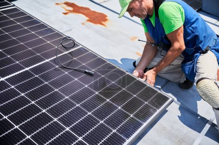 Téléchargez les photos : Travailleur construction système de panneaux solaires sur le toit métallique de la maison. Homme ingénieur installant le module solaire photovoltaïque à l'extérieur. Concept de production d'énergies alternatives, vertes et renouvelables. - en image libre de droit