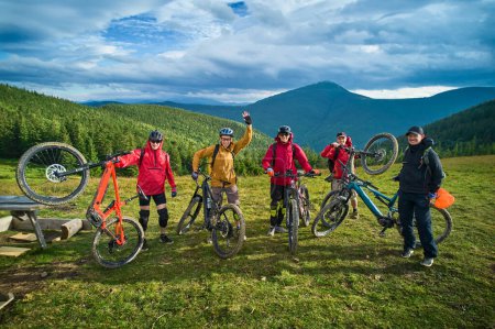 Téléchargez les photos : Groupe de cyclistes hommes en vélo électrique à l'extérieur. Portrait de touristes heureux reposant sur le sommet de la colline, jouissant d'un beau paysage de montagne. Concept de sport, loisirs actifs et nature. - en image libre de droit
