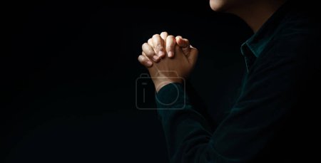 Foto de Concepto Espiritualidad, Religión y Esperanza. Persona haciendo manos a la oración en el cuarto oscuro. Símbolo de humildad, súplica, creencia y fe. Tono oscuro. Enfoque recortado y selectivo - Imagen libre de derechos