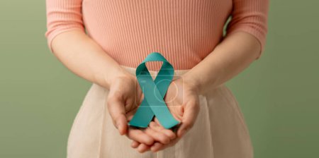 Photo for Ovarian and Cervical Cancer Awareness. Woman Holding Teal Ribbon on Lower Abdomen, Uterus, Female Reproductive System, Women's Health, PCOS and Gynecology - Royalty Free Image