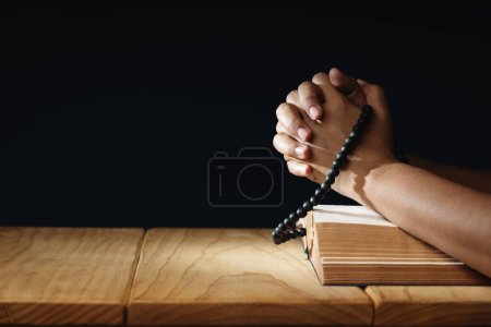 Photo for Spirituality, Religion and Hope Concept. Person Praying by Holy Bible and Bead on Desk. Symbol of Humility, Supplication, Believe and Faith for Christian People. Dark Tone. - Royalty Free Image