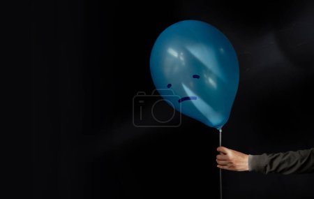 Photo for Mental Health Disorder Concept. a Stressed, Anxiety, Depressed Person Holding a Blue Balloon with a Sadness Face from the Dark , Negative Emotion and Feeling. Moody. Dark tone - Royalty Free Image