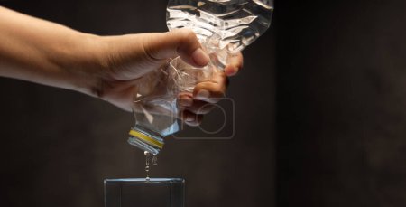 Photo for Water Crisis, Climate Change, El Nino, Global Warming Issue Concept. Hand trying to Squeeze Water from a bottle to a Glass - Royalty Free Image
