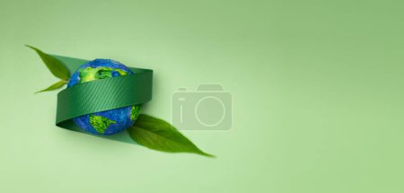 Photo for World Earth Day Concept. Plant a Tree on the Planet, ESG, Renewable and Sustainable Resources. Environmental Care. Green Ribbon and Leaf Embracing a Globe. Top View - Royalty Free Image