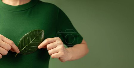 Photo for Green Energy, ESG, Renewable and Sustainable Resources. Environmental and Ecology Care Concept. Close up of Hand Holding a Green Leaf on Chest - Royalty Free Image