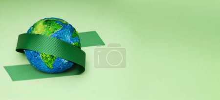 Photo for World Earth Day Concept. Green Energy, ESG, Renewable and Sustainable Resources. Environmental Care. Green Ribbon Embracing a Globe. Top View - Royalty Free Image