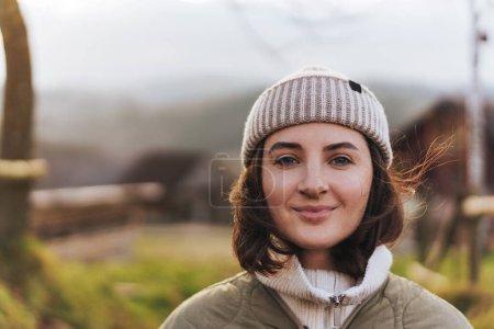 Téléchargez les photos : Portrait de jeune voyageuse en vacances. Joyeux sourire fille portant bonnet chapeau regardant la caméra sur fond de coucher de soleil. - en image libre de droit