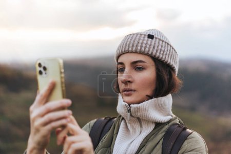 Téléchargez les photos : Portrait de voyageuse utilisant un téléphone cellulaire avec carte en ligne et textos à des amis, forêt floue et montagnes en arrière-plan, concept d'utilisation des technologies dans la nature - en image libre de droit