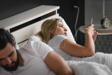 Foto de Pareja de adultos jóvenes que utilizan teléfonos inteligentes en la cama adictos a las redes sociales. Concepto de adicción móvil - Imagen libre de derechos
