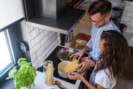 Téléchargez les photos : Heureux couple multiethnique cuisinant des tomates maison et des pâtes au basilic. Cuisiner à la maison - en image libre de droit