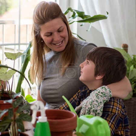 Téléchargez les photos : Mère et fils rempoter des plantes ensemble dans le jardin de la maison. Jardinage printanier. - en image libre de droit