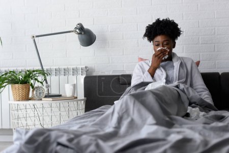 Foto de Joven mujer afroamericana acostada en la cama en casa. Sensación de malestar con gripe o coronavirus - Imagen libre de derechos